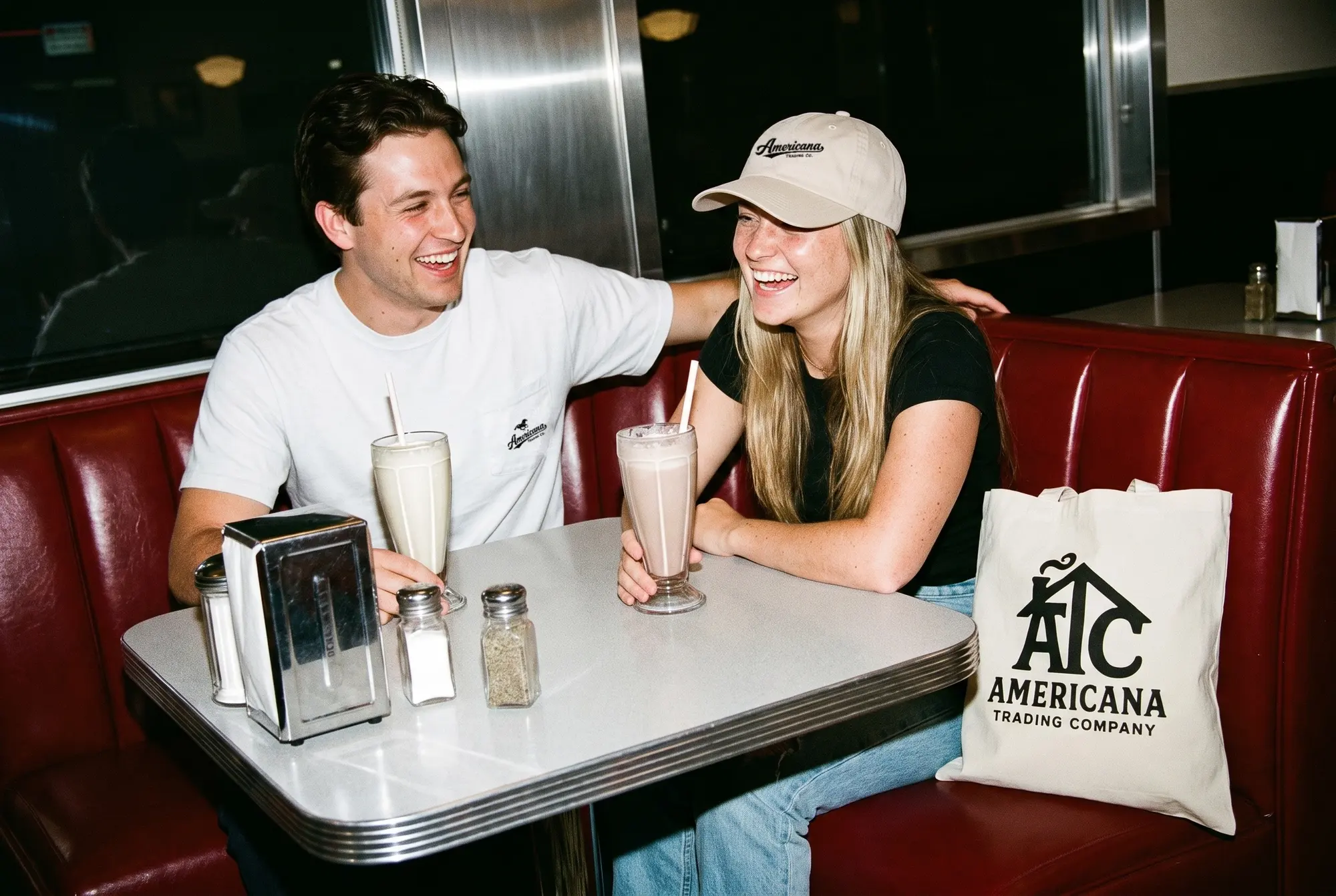 Two people in a diner booth, one in a Harvest Tee and one in a Horse Pocket Tee.